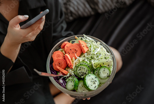 Woman in bed with phone and fresh vegetable salad.