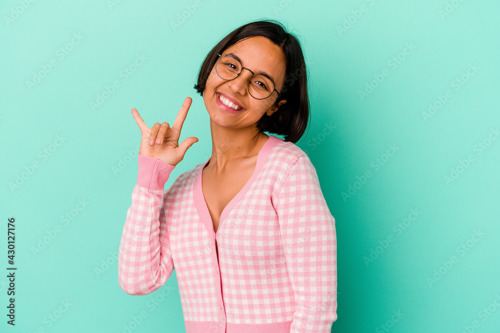 Young mixed race woman isolated on blue background showing a horns gesture as a revolution concept.
