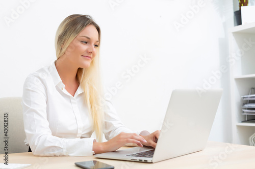 Attractive young Caucasian businesswoman smiling working in front of computer in office.