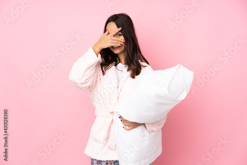 Young woman in pajamas isolated on pink background covering eyes by hands and smiling