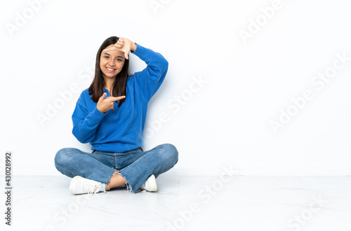 Young mixed race woman sitting on the floor isolated on white background focusing face. Framing symbol