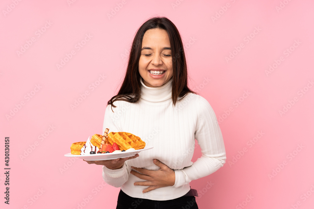 Young brunette woman holding waffles over isolated pink background smiling a lot