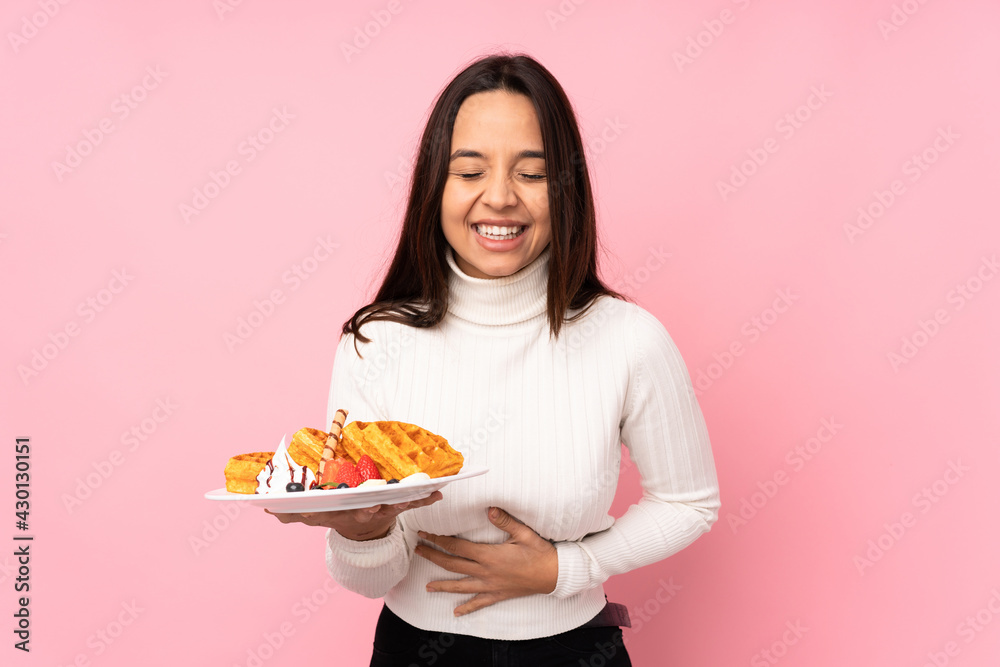 Young brunette woman holding waffles over isolated pink background smiling a lot Young brunette woman holding waffles over isolated pink background smiling a lot