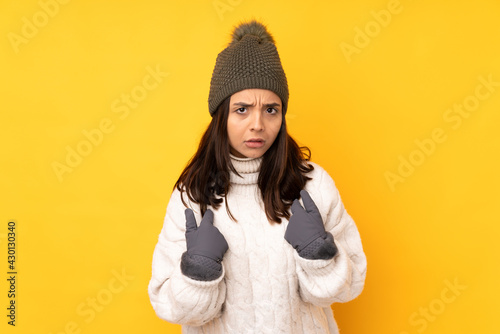 Young woman with winter hat over isolated yellow background pointing to oneself © luismolinero