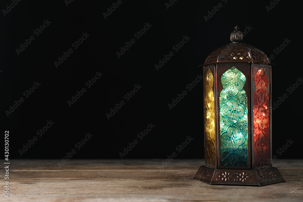 Decorative Arabic lantern on wooden table against black background, space for text - obrazy, fototapety, plakaty 