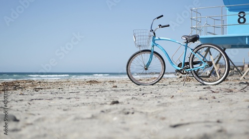 Blue bicycle, cruiser bike by ocean beach, pacific coast, Oceanside California USA. Summertime vacations, sea shore. Vintage cycle on sand near lifeguard tower or watchtower hut. Sky and water waves.
