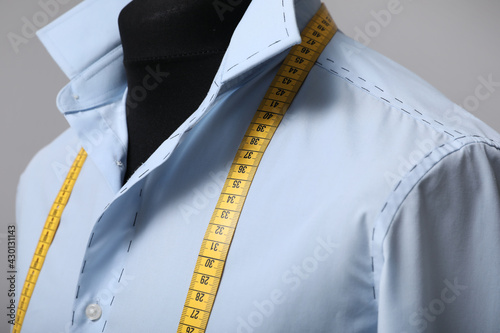 Semi-ready shirt with tailor's measuring tape on mannequin against grey background, closeup