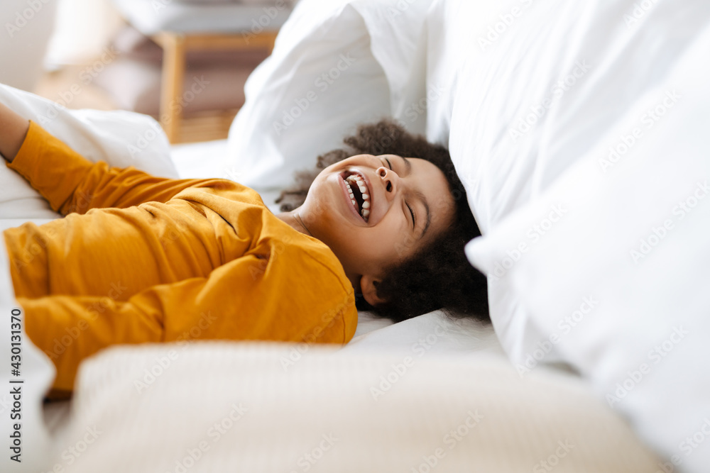 Black curly boy laughing while making fun in bed at home Black curly boy laughing while making fun in bed at home