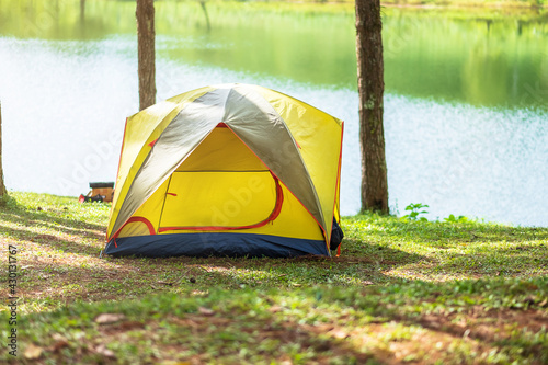 Camping under the forest, yellow tent near lake. Outdoor travel, trip and vacation concept