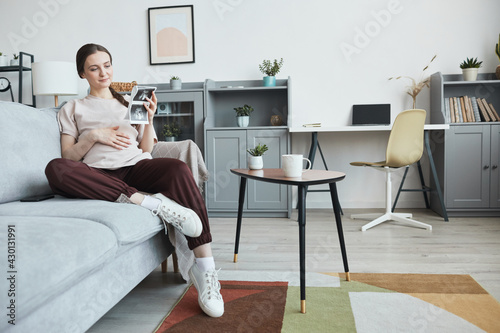 Pregnant woman resting on sofa with x-ray image of her baby in the living room