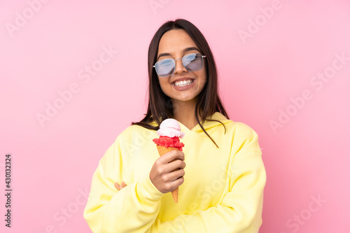 Young brunette girl holding a cornet ice cream over isolated pink background looking up while smiling