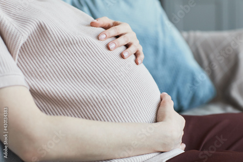 Close-up of pregnant woman in shirt stroking her belly sitting on sofa