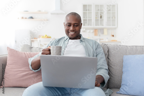 Wallpaper Mural Reading morning news. Happy african american man using laptop and drinking hot coffee, resting on sofa Torontodigital.ca