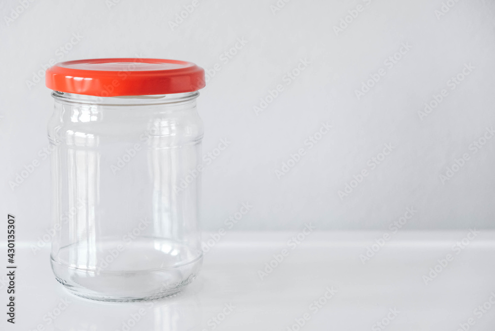 Empty glass jar with red cover on white table background. Copy, empty space for text Empty glass jar with red cover on white table background. Copy, empty space for text