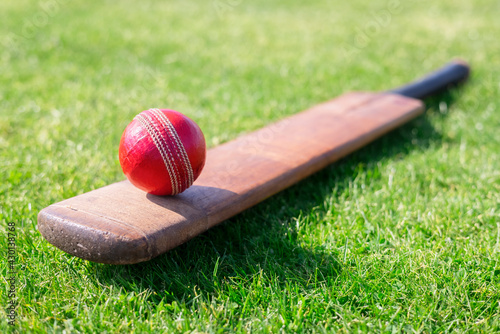 Cricket ball on top of cricket bat on green grass of cricket pitch photo