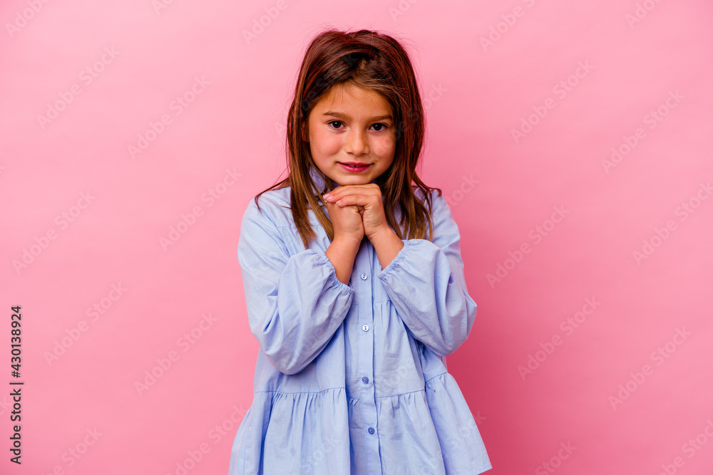 Little caucasian girl isolated on pink background keeps hands under chin, is looking happily aside. Little caucasian girl isolated on pink background keeps hands under chin, is looking happily aside.