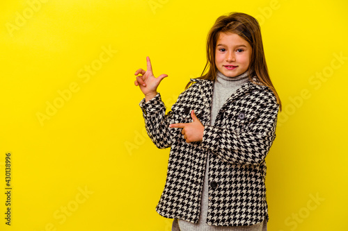 Little caucasian girl isolated on yellow background excited pointing with forefingers away.