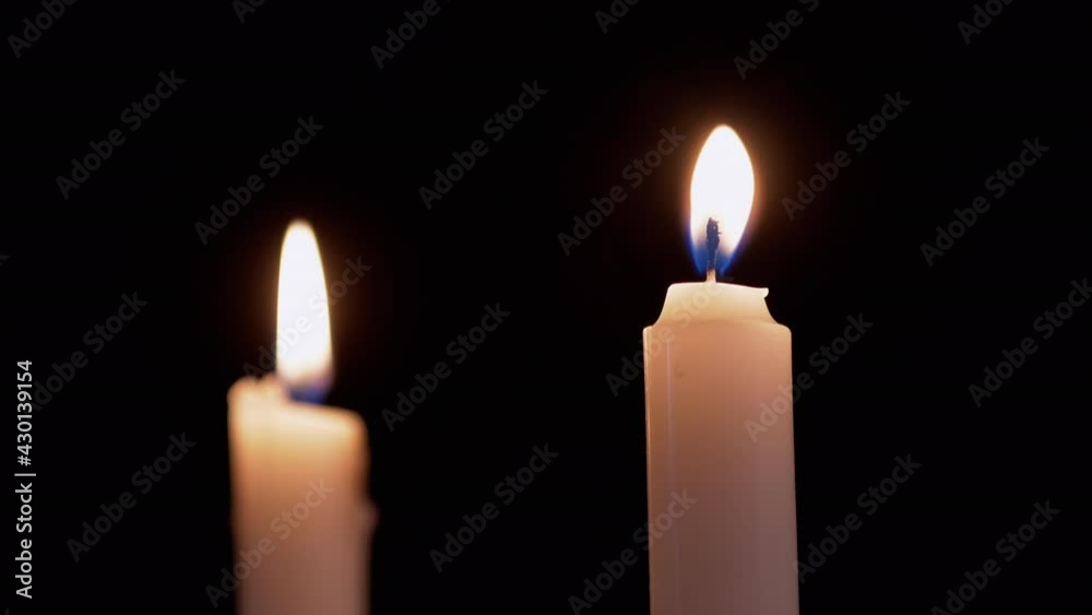 Two White Paraffin Candles Burn with Yellow Fire, on a Black Background. Wax candles with a bright moving flame, fire in smoke. Concept of memory, ritual, celebration. Church rites. 4K Two White Paraffin Candles Burn with Yellow Fire, on a Black Background. Wax candles with a bright moving flame, fire in smoke. Concept of memory, ritual, celebration. Church rites. 4K