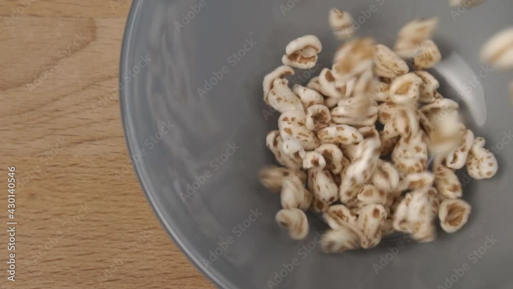 Uncooked cereal puffed spelt wheat fall and fill a gray bowl close-up on a wooden cutting board in slow motion Uncooked cereal puffed spelt wheat fall and fill a gray bowl close-up on a wooden cutting board in slow motion
