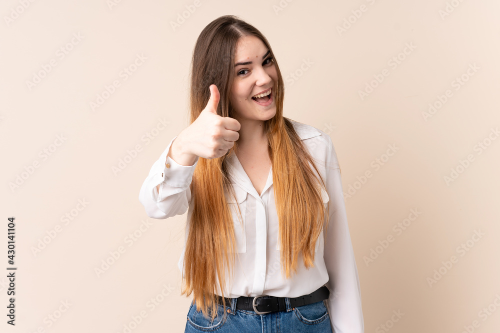 Young caucasian woman isolated on beige background with thumbs up because something good has happened Young caucasian woman isolated on beige background with thumbs up because something good has happened