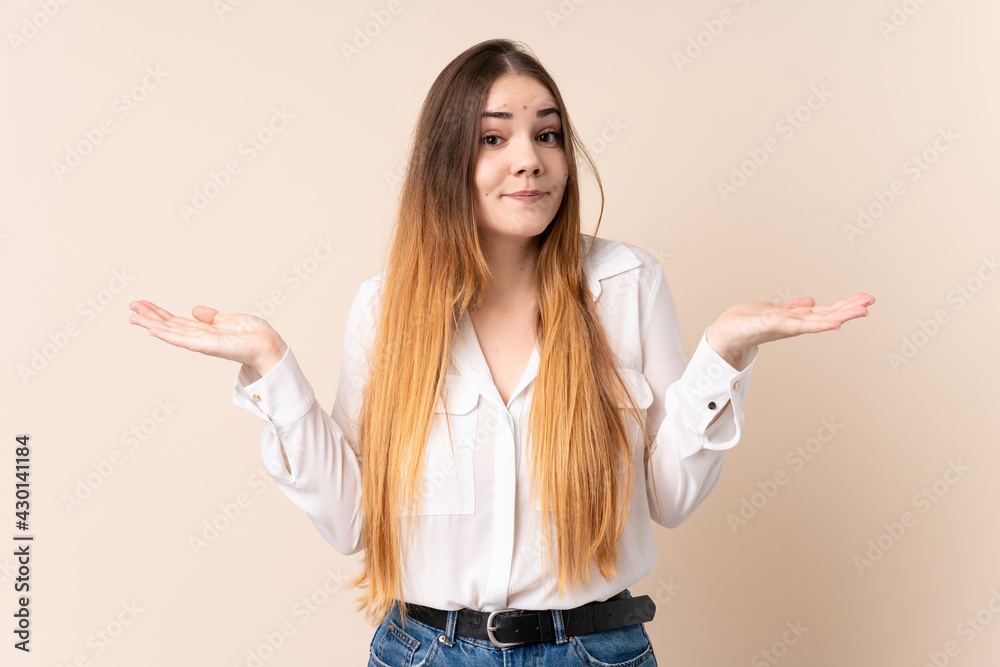 Young caucasian woman isolated on beige background making doubts gesture Young caucasian woman isolated on beige background making doubts gesture