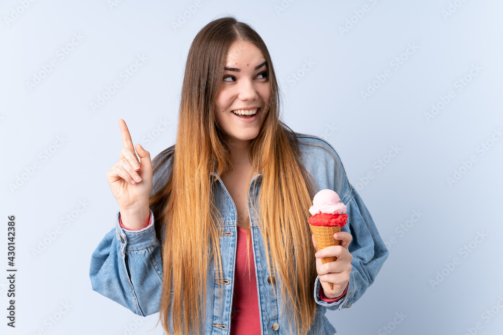 Young woman with a cornet ice cream isolated on blue background intending to realizes the solution while lifting a finger up Young woman with a cornet ice cream isolated on blue background intending to realizes the solution while lifting a finger up