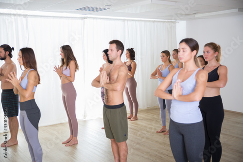 Group of young sporty attractive people in yoga studio, practicing yoga lesson with instructor, standing, stretching and relaxing after workout . Healthy active lifestyle, working out indoors in gym