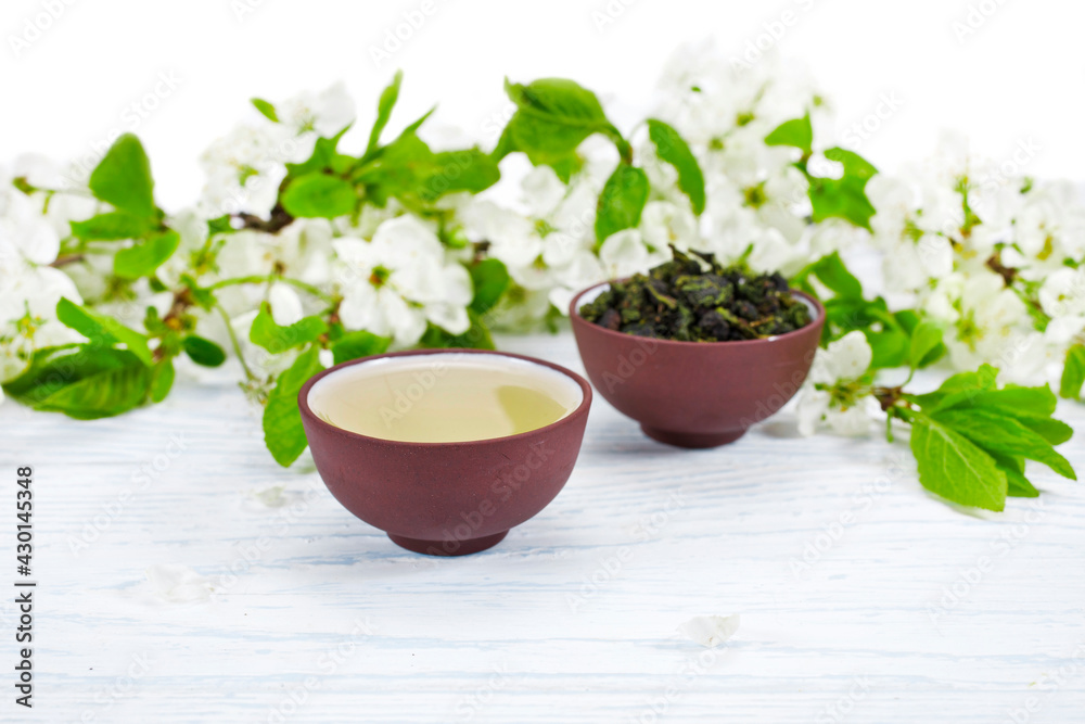Green oolong tieguanyin tea in the ceramic cups with branches of blossoming cherry tree on white wooden background. Spring tea ceremony. Green oolong tieguanyin tea in the ceramic cups with branches of blossoming cherry tree on white wooden background. Spring tea ceremony.