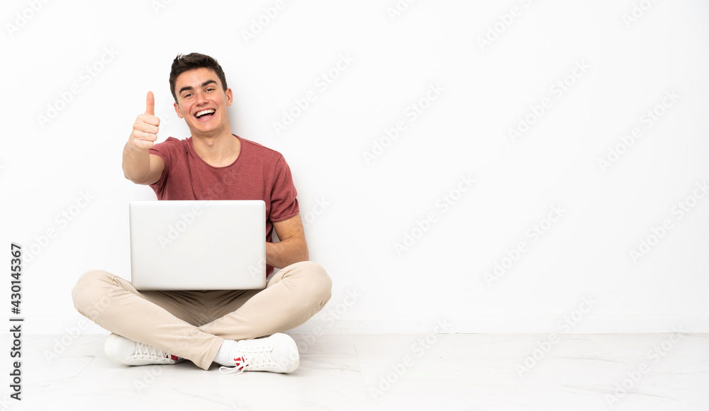 Teenager man sitting on the flor with his laptop with thumbs up because something good has happened Teenager man sitting on the flor with his laptop with thumbs up because something good has happened