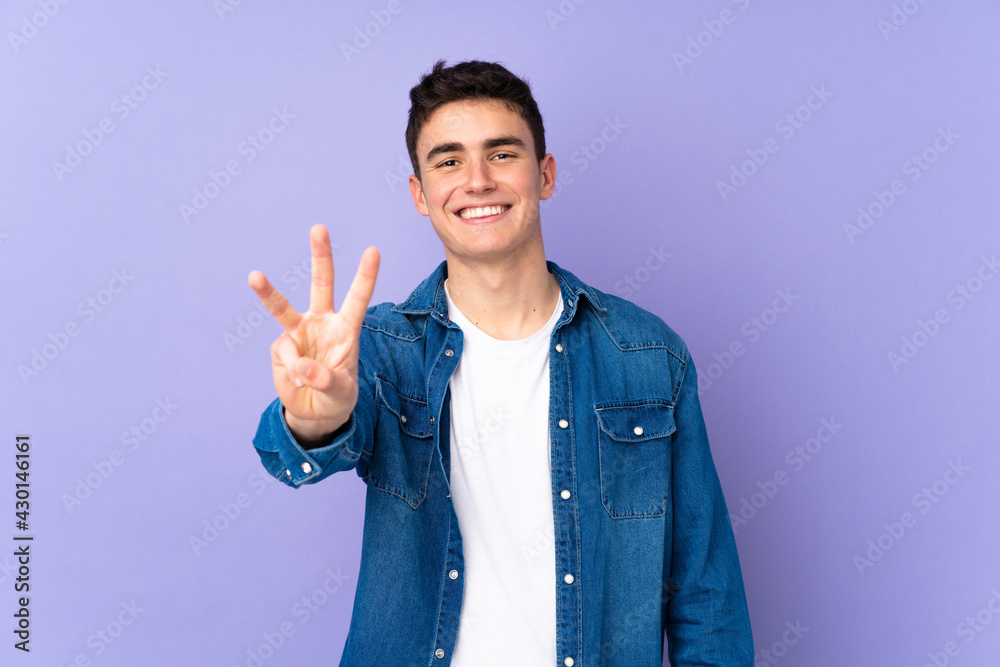 Teenager caucasian handsome man isolated on purple background happy and counting three with fingers Teenager caucasian handsome man isolated on purple background happy and counting three with fingers