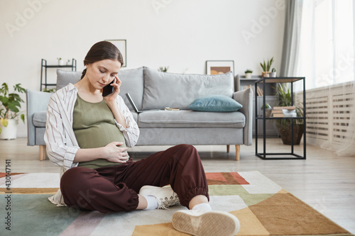 Pregnant woman sitting on the floor and talking on mobile phone in the living room photo