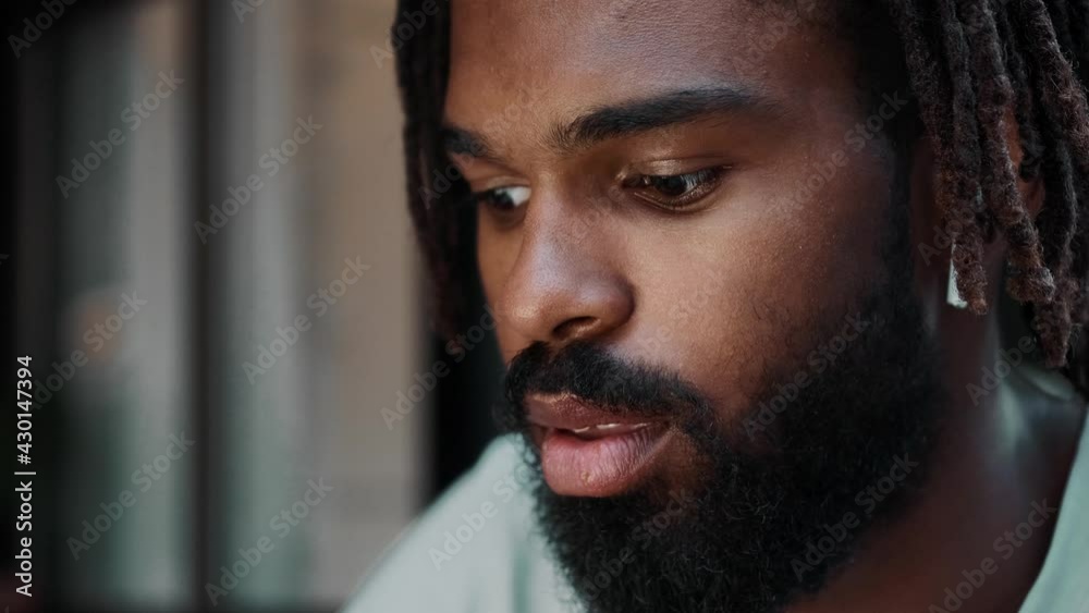 A close-up view of a handsome african american man with earbuds is using his laptop while sitting on the street A close-up view of a handsome african american man with earbuds is using his laptop while sitting on the street
