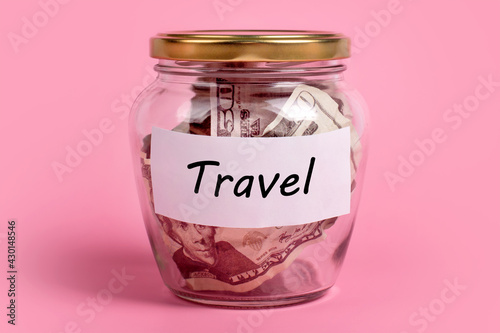 Money box with word TRAVEL on sticky note paper. Dollars in glass jar with savings label, financial, saving. Jar full of american dollar bills, cash, save money concept, expense planning, control. photo