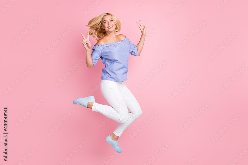 Full length body size view of lovely cheerful wavy-haired girl jumping showing v-sign isolated over pink pastel color background
