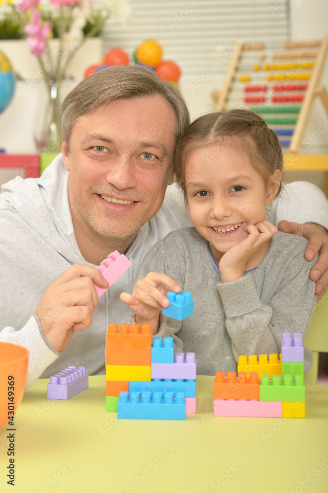 Father and cute little daughter sitting at table and playing with colorful plastic blocks Father and cute little daughter sitting at table and playing with colorful plastic blocks