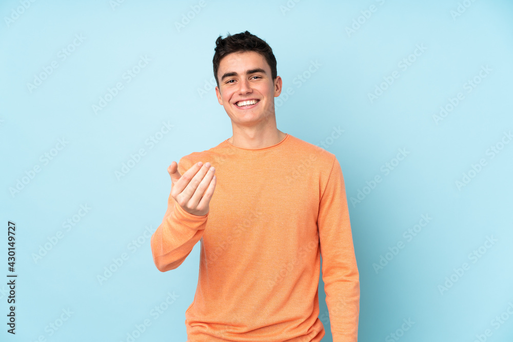 Teenager caucasian handsome man isolated on purple background inviting to come Teenager caucasian handsome man isolated on purple background inviting to come