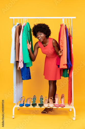 Joyful African Woman Posing Among Hangers On Clothing Rail, Studio