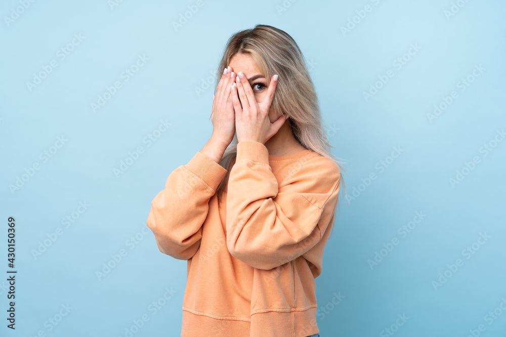 Teenager girl over isolated blue background covering eyes and looking through fingers