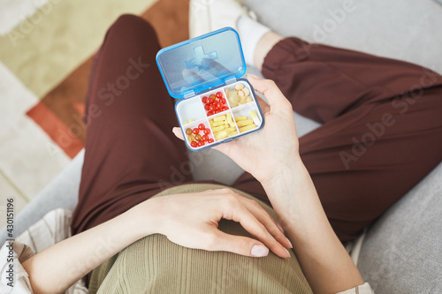 High angle view of pregnant woman holding box with vitamins and pills while sitting on sofa