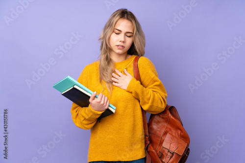 Teenager Russian student girl isolated on purple background having a pain in the heart