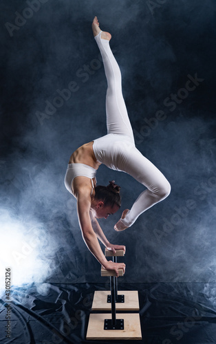 Flexible circus artist - female acrobat doing handstand on the back and smoker background