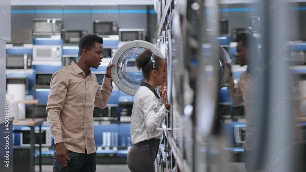cheerful afro-american couple is choosing washing machine in hardware shop, man and woman are viewing new models inside cheerful afro-american couple is choosing washing machine in hardware shop, man and woman are viewing new models inside
