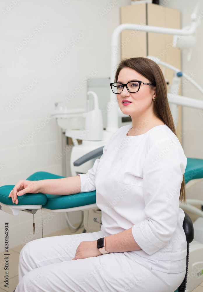 a woman doctor with brown hair glasses and a white suit is sitting in the office near the couch a woman doctor with brown hair glasses and a white suit is sitting in the office near the couch