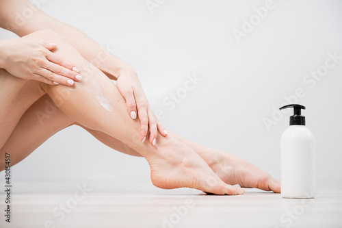Woman applies moisturizer to her legs on a white background. The girl takes care of the skin and uses the cream