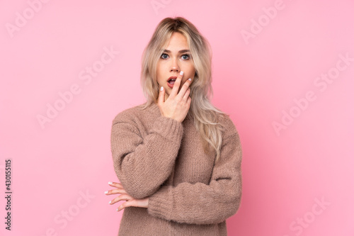 Teenager blonde girl wearing a sweater over isolated pink background surprised and shocked while looking right