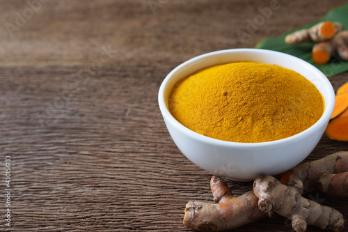  Turmeric powder in a white bowl and fresh turmeric (curcumin) on wooden background,Used for cooking,herbal,copy space.
