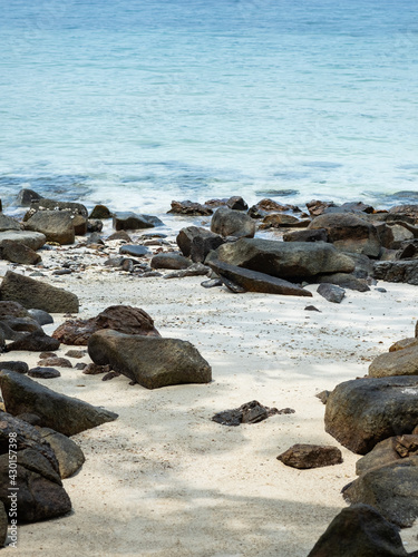 Sandy beach with a rocks in the shade of the trees, blue ocean background.