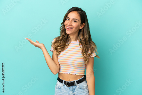 Bild auf Leinwand Young woman over isolated blue background holding copyspace imaginary on the pal
