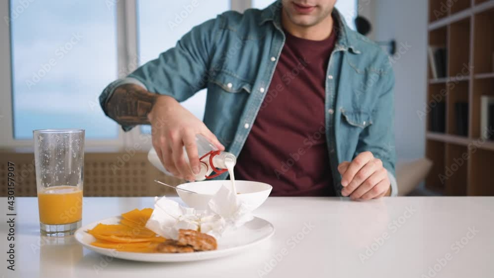 A cropped view of a man is pouring milk to the bowl with muesli while having breakfast at home A cropped view of a man is pouring milk to the bowl with muesli while having breakfast at home
