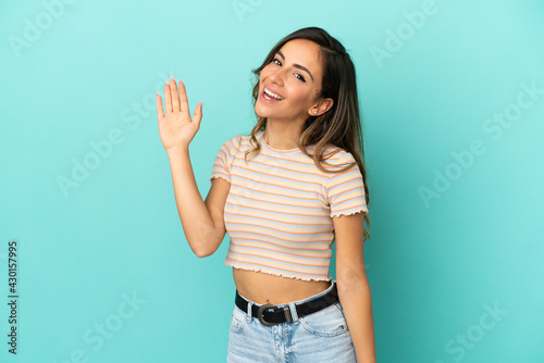 Young woman over isolated blue background saluting with hand with happy expression